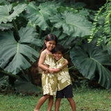 little girl wearing spaghetti strap dress in green print with naupaka pattern