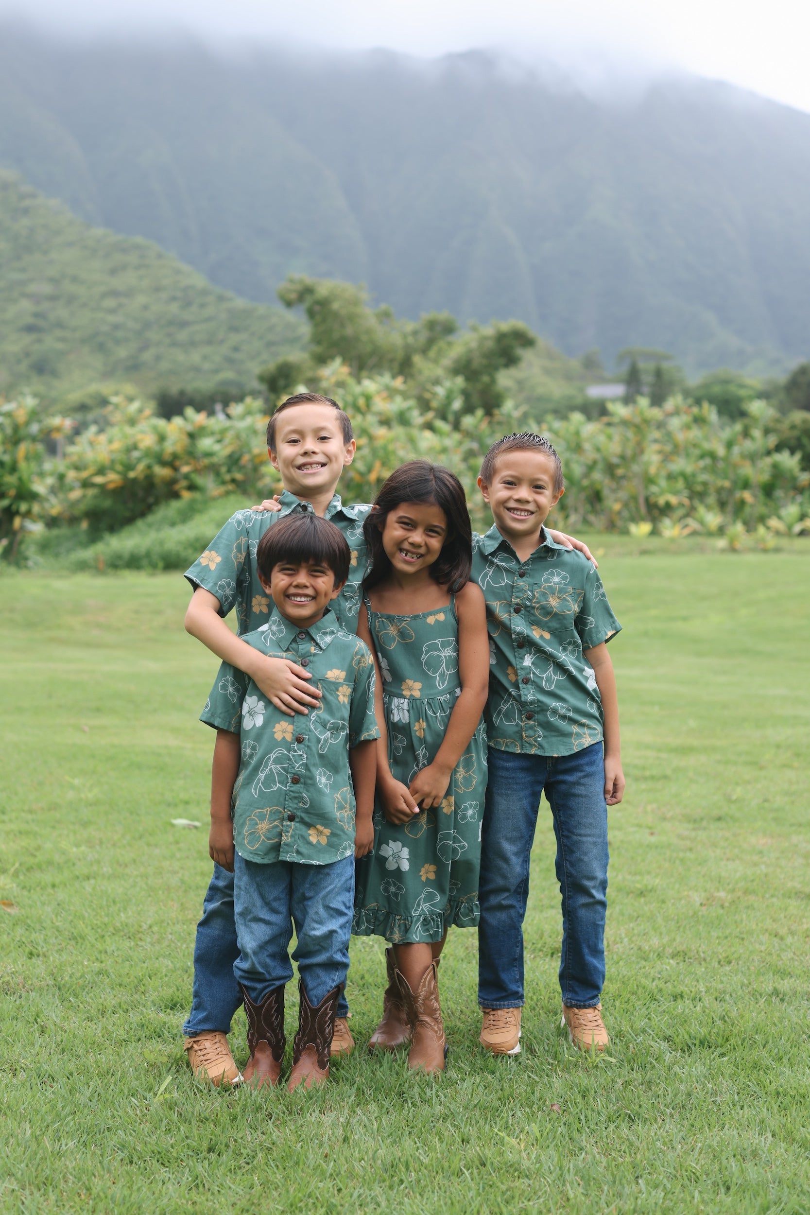 little boy wearing lush green aloha button up shirt with pua kenikeni print