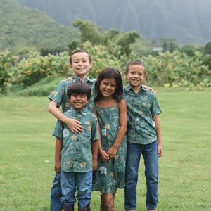 little boy wearing lush green aloha button up shirt with pua kenikeni print