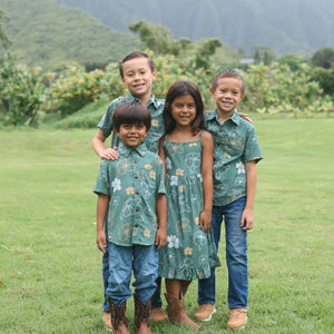 little girl wearing lush green tie back dress with puakenikeni print