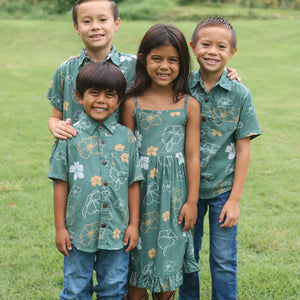 little girl wearing lush green tie back dress with puakenikeni print