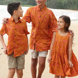 little girl wearing an orange flowy dress with puakenikeni print