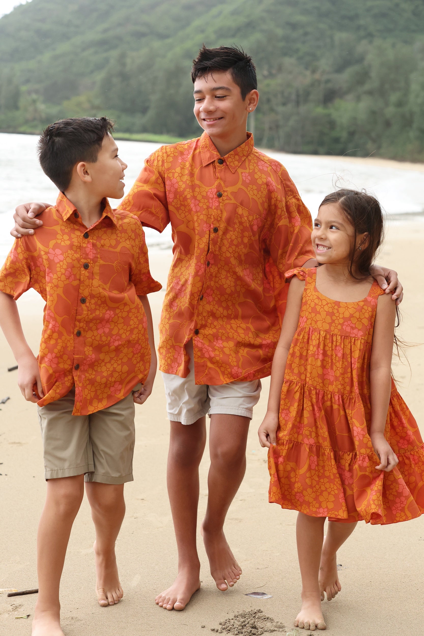 little girl wearing an orange flowy dress with puakenikeni print