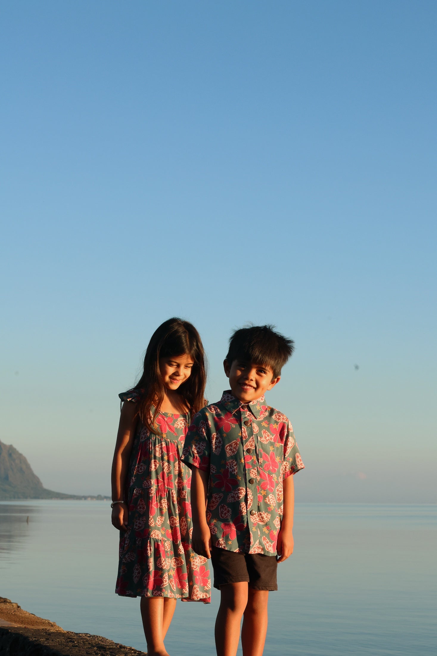 little boy wearing a teal aloha shirt with shell and pua print 