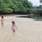 little boy wearing board shorts  in blush and brown hibiscus print.