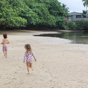 little boy wearing board shorts  in blush and brown hibiscus print.