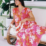 woman with brown hair wearing a pink short sleeve tiered maxi dress with retro flower print