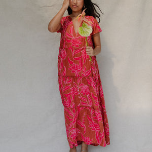 woman with brown hair wearing a sienna colored maxi v neck dress with awapuhi pattern