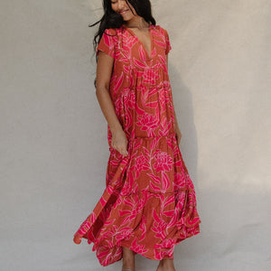 woman with brown hair wearing a sienna colored maxi v neck dress with awapuhi pattern