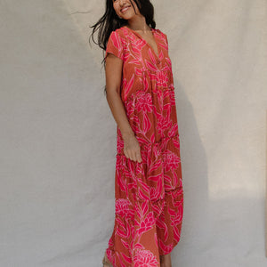 woman with brown hair wearing a sienna colored maxi v neck dress with awapuhi pattern