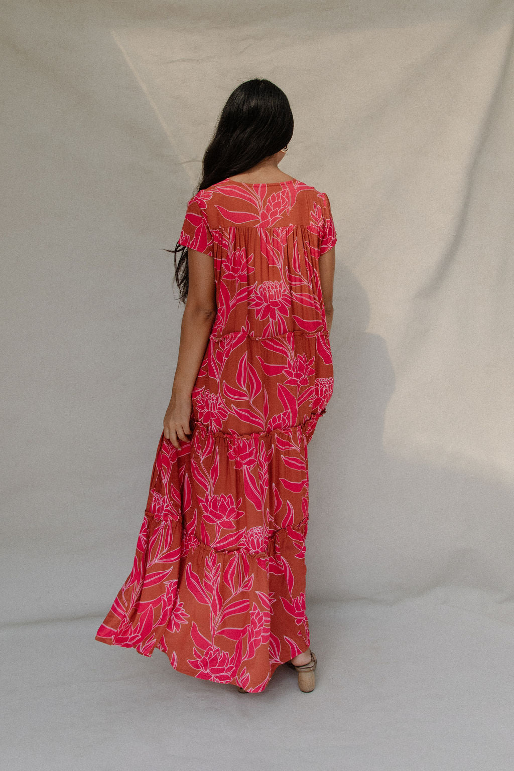 woman with brown hair wearing a sienna colored maxi v neck dress with awapuhi pattern