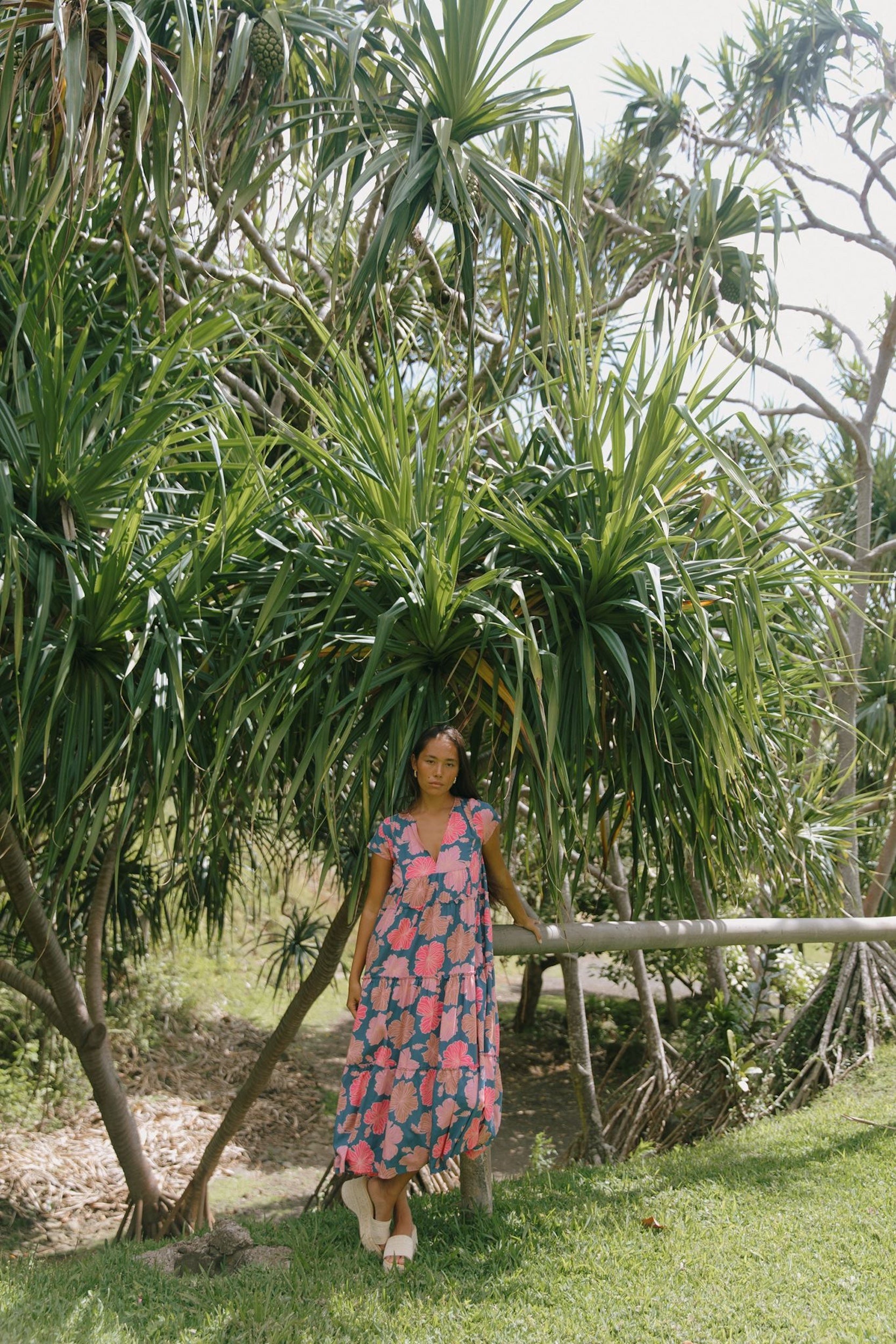 woman with brown hair wearing a navy maxi dress with bright pink hibiscus