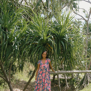 woman with brown hair wearing a navy maxi dress with bright pink hibiscus