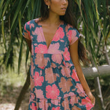 woman with brown hair wearing a navy maxi dress with bright pink hibiscus