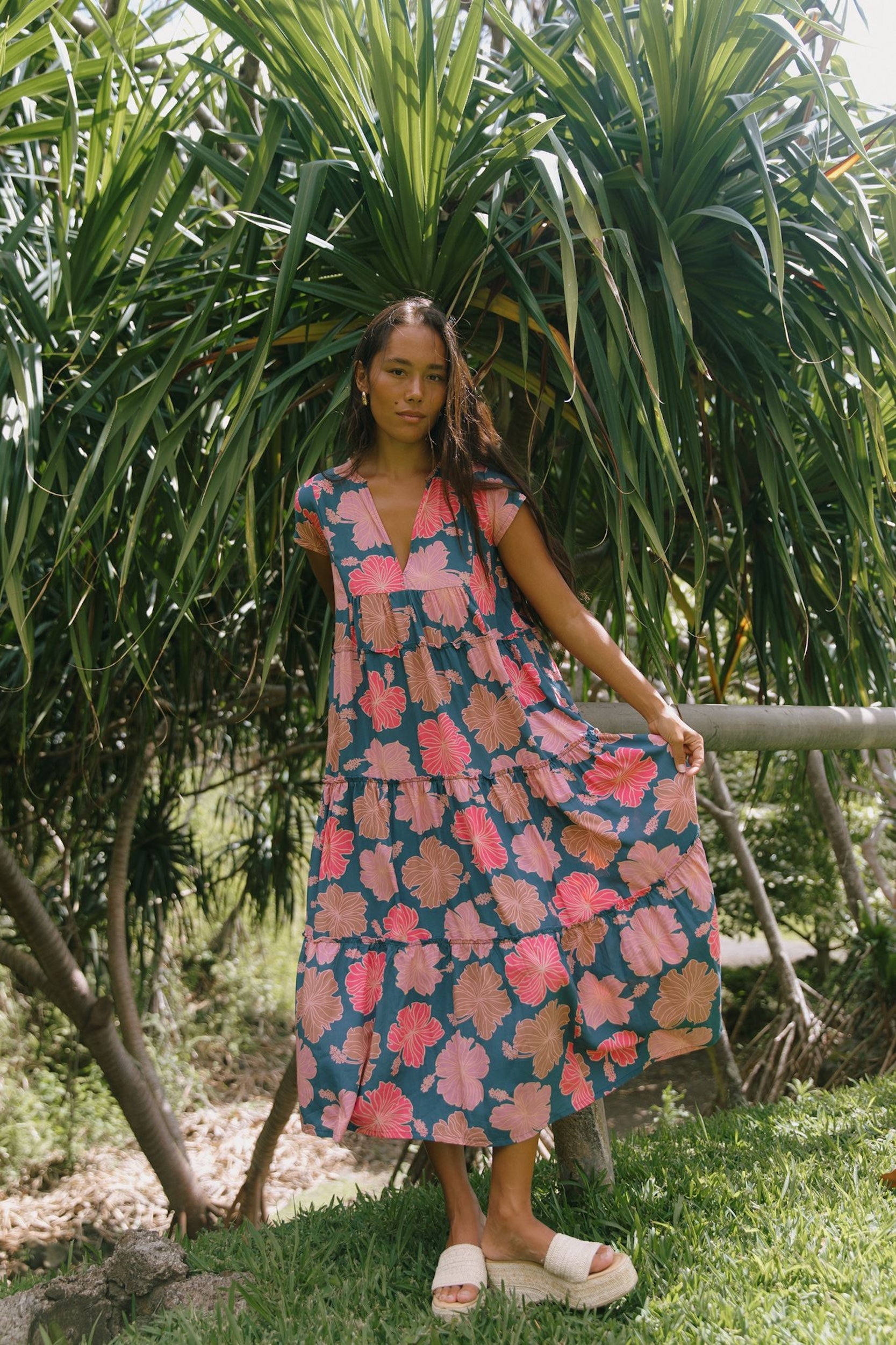 woman with brown hair wearing a navy maxi dress with bright pink hibiscus