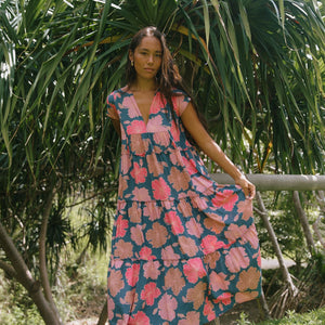 woman with brown hair wearing a navy maxi dress with bright pink hibiscus