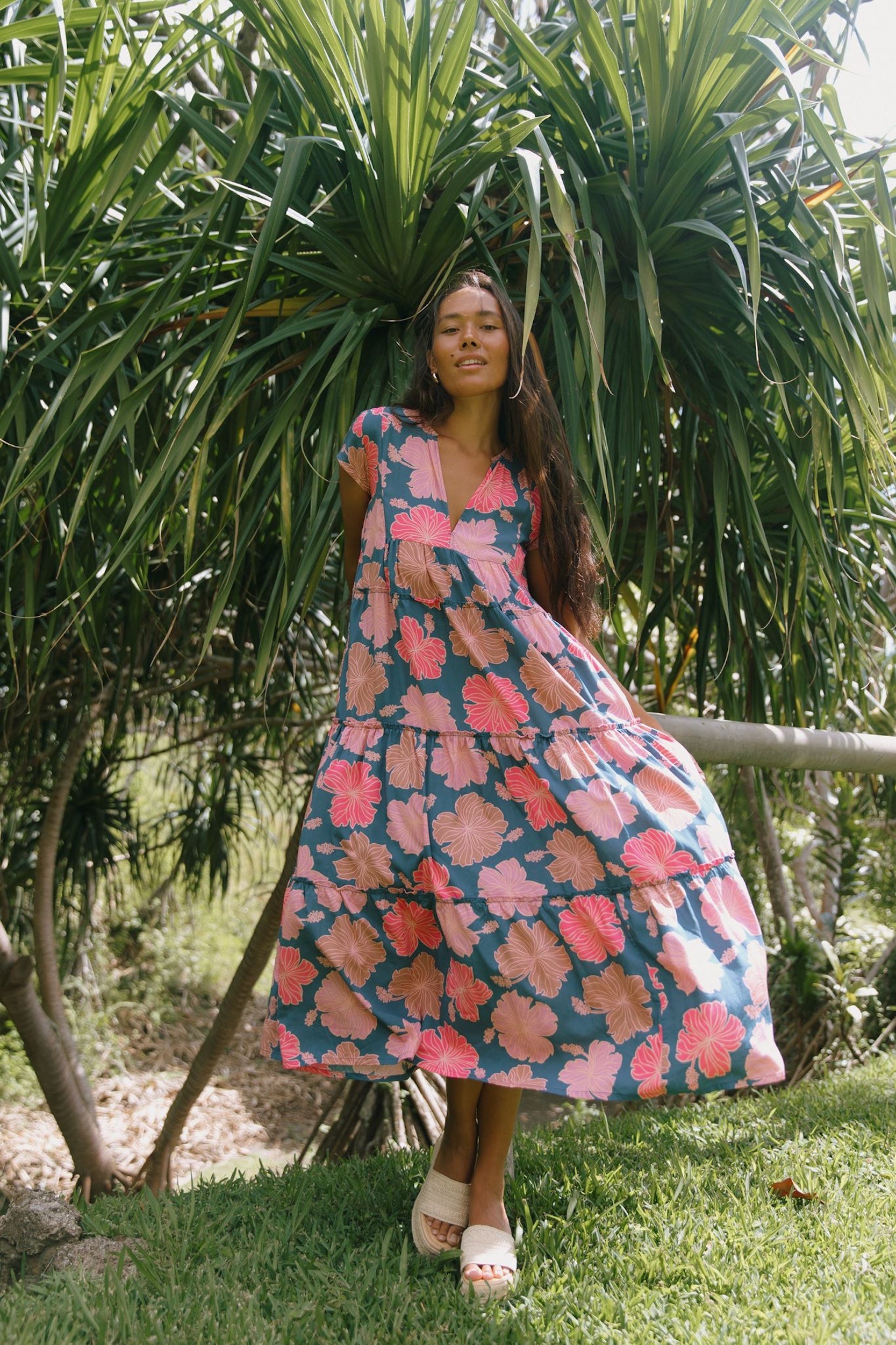 woman with brown hair wearing a navy maxi dress with bright pink hibiscus