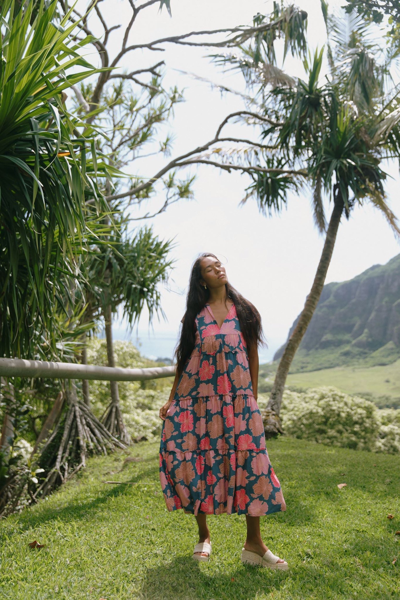 woman with brown hair wearing a navy maxi dress with bright pink hibiscus