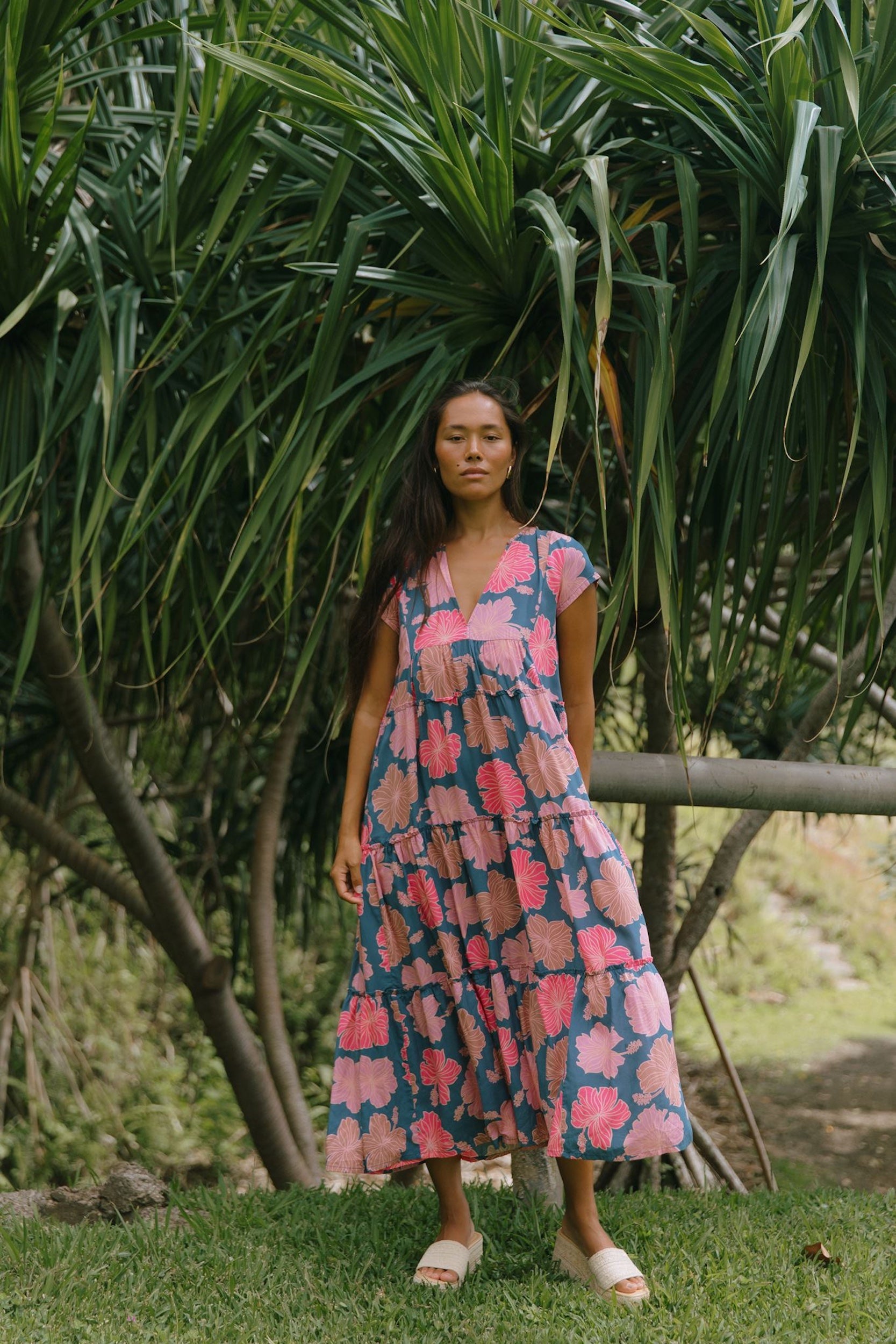 woman with brown hair wearing a navy maxi dress with bright pink hibiscus