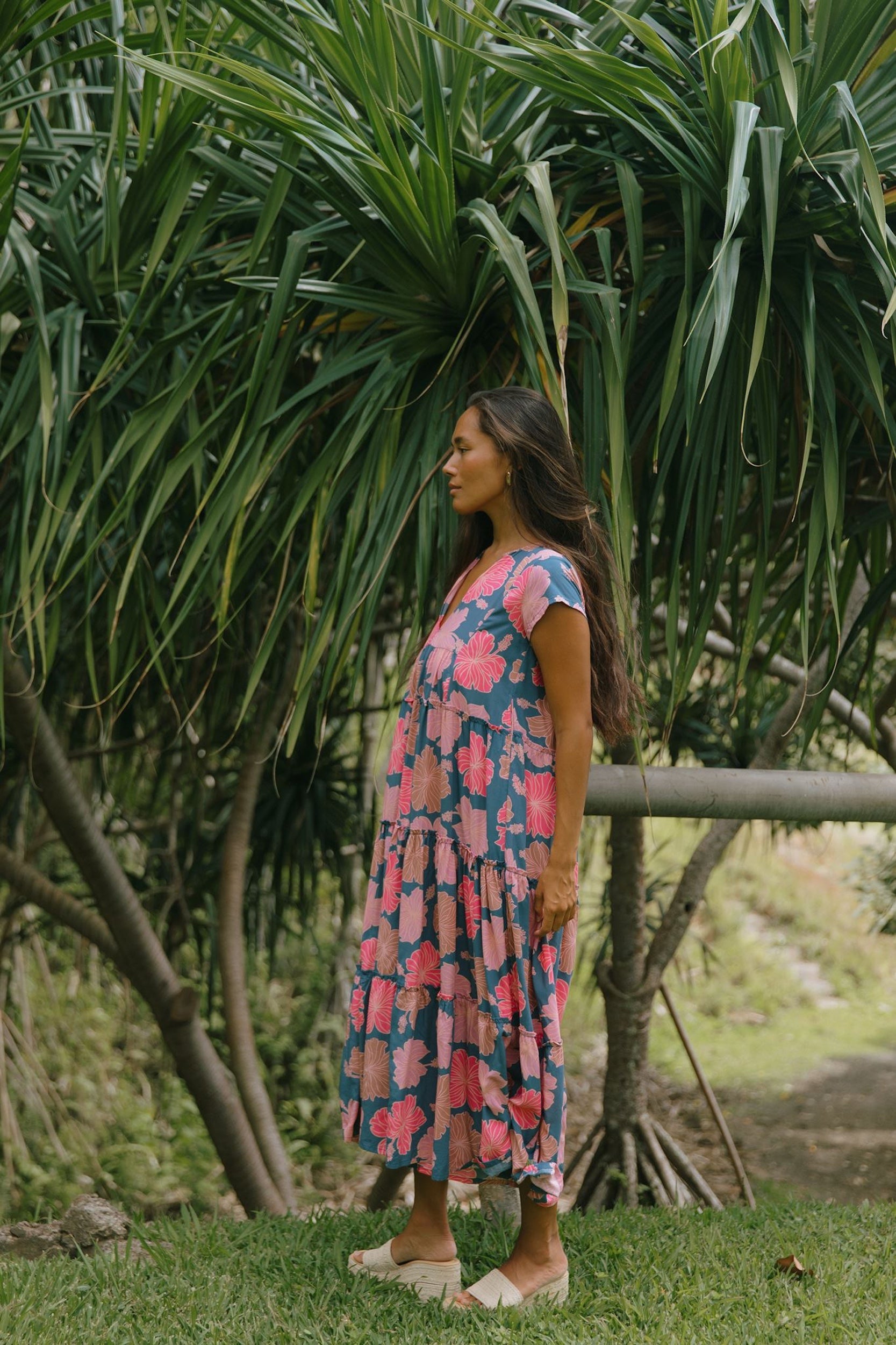 woman with brown hair wearing a navy maxi dress with bright pink hibiscus