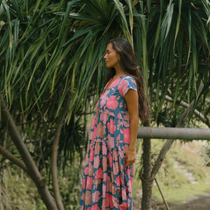 woman with brown hair wearing a navy maxi dress with bright pink hibiscus