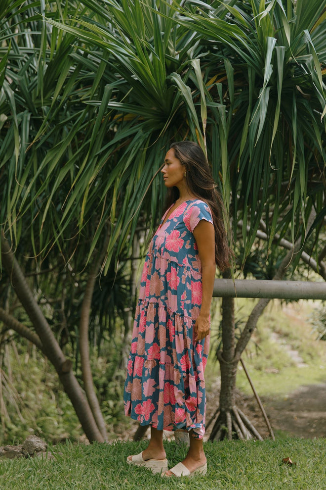 woman with brown hair wearing a navy maxi dress with bright pink hibiscus
