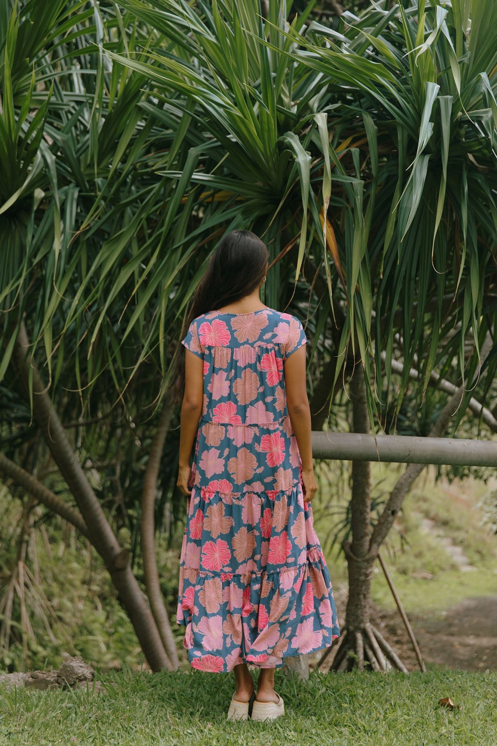 woman with brown hair wearing a navy maxi dress with bright pink hibiscus