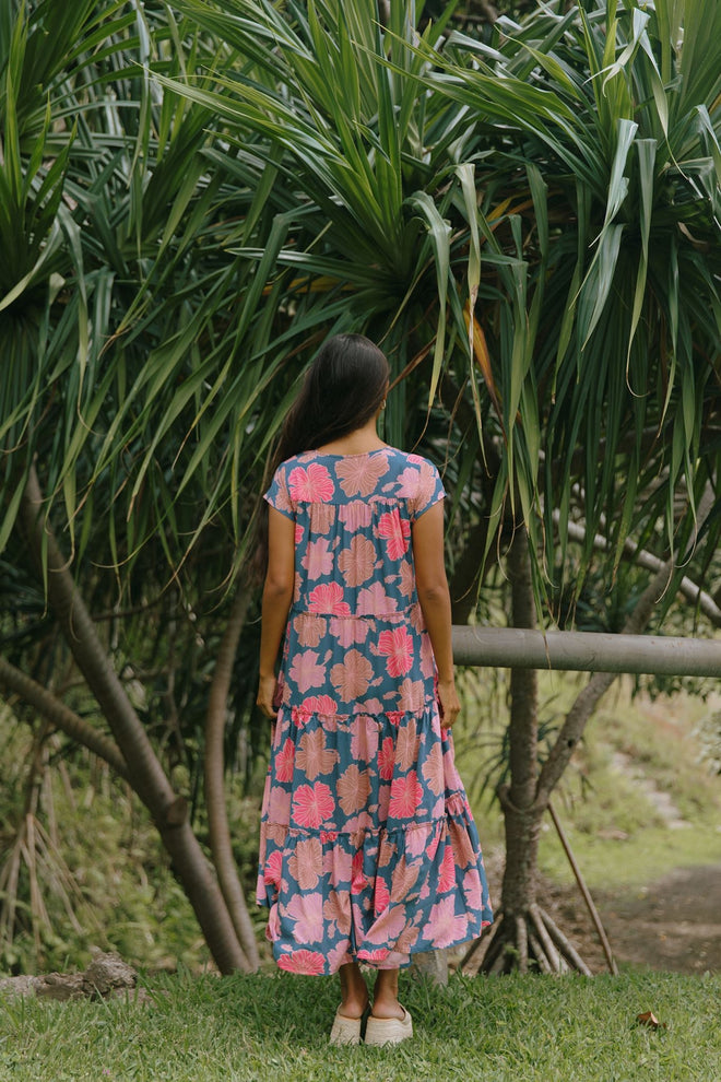 woman with brown hair wearing a navy maxi dress with bright pink hibiscus