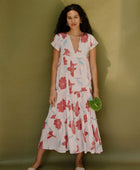 Woman wearing long flowy tiered short sleeve dress with red and light blue floral on beige ground.