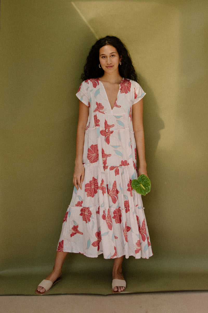 Woman wearing long flowy tiered short sleeve dress with red and light blue floral on beige ground.