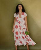 Woman wearing long flowy tiered short sleeve dress with red and light blue floral on beige ground.