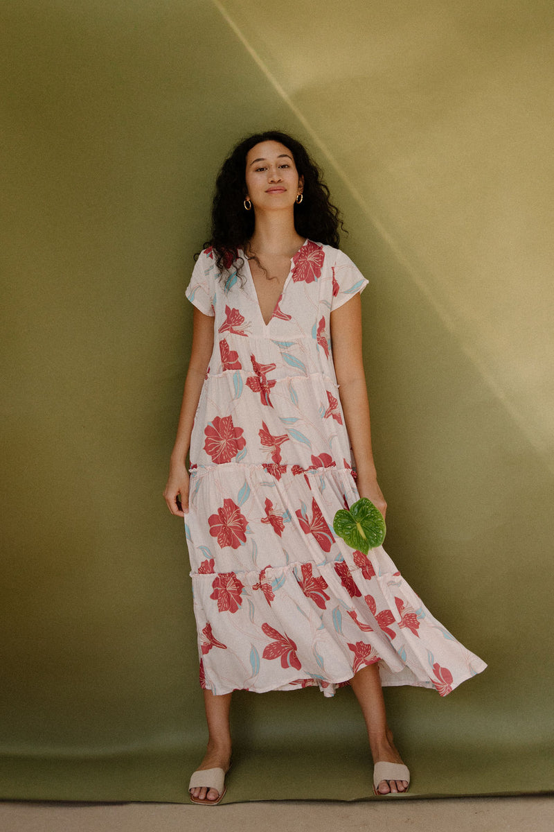 Woman wearing long flowy tiered short sleeve dress with red and light blue floral on beige ground.