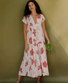 Woman wearing long flowy tiered short sleeve dress with red and light blue floral on beige ground.