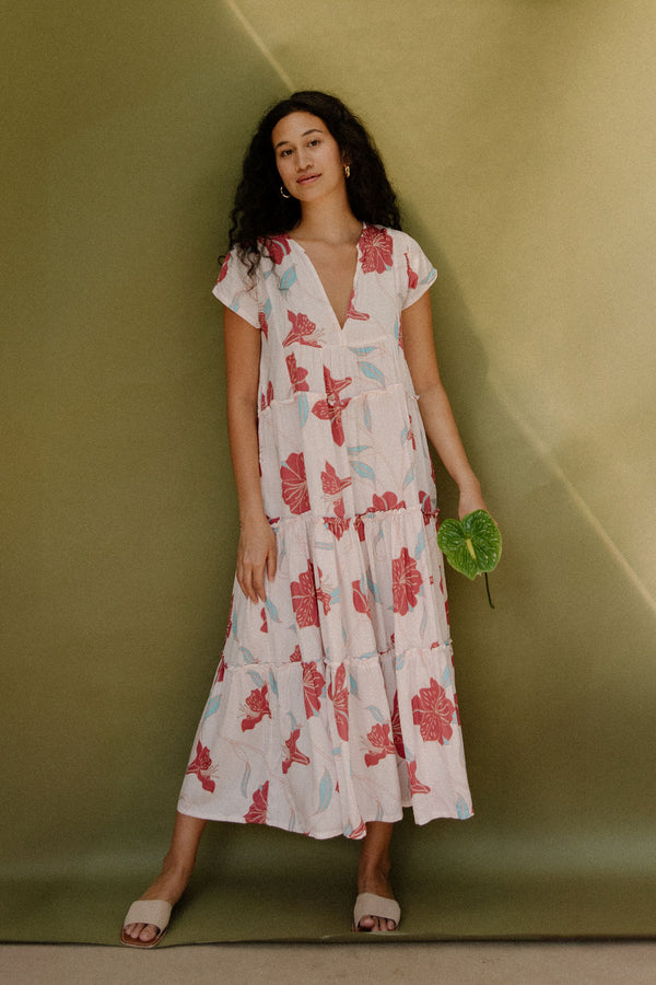 Woman wearing long flowy tiered short sleeve dress with red and light blue floral on beige ground.