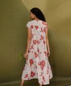 Woman wearing long flowy tiered short sleeve dress with red and light blue floral on beige ground.