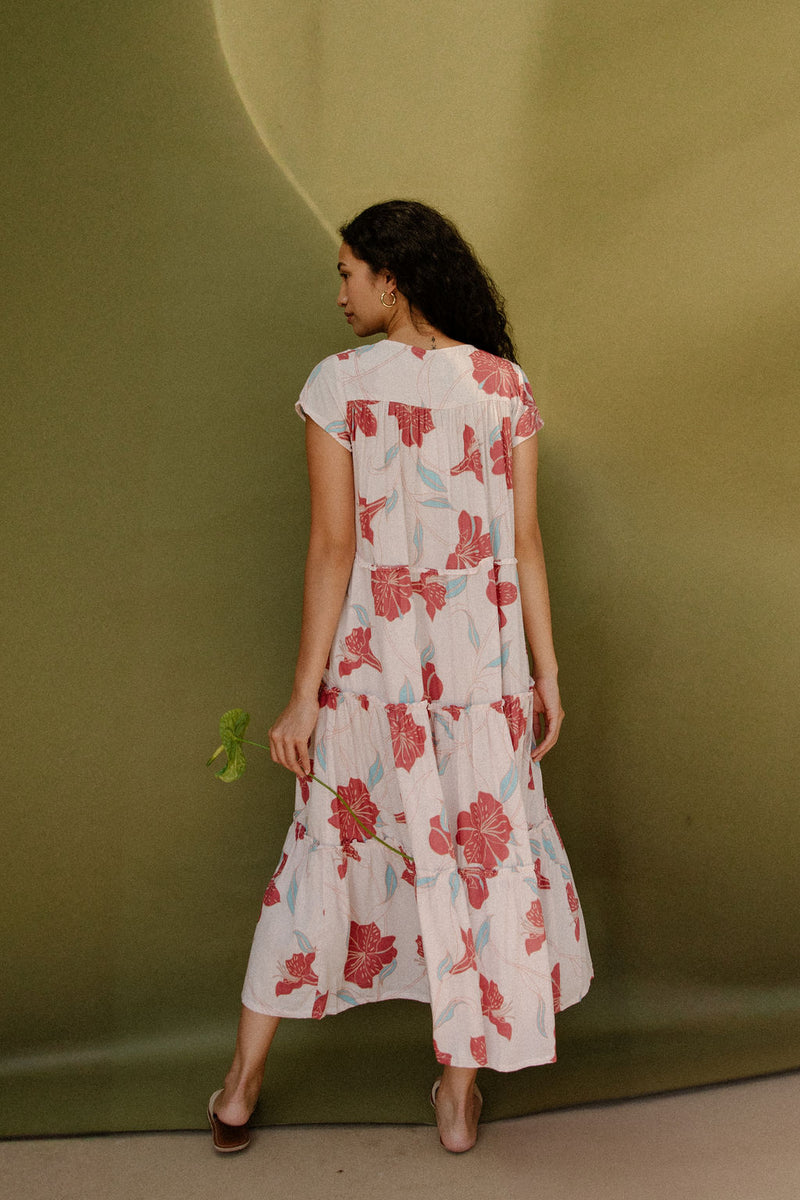 Woman wearing long flowy tiered short sleeve dress with red and light blue floral on beige ground.