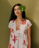 Woman wearing long flowy tiered short sleeve dress with red and light blue floral on beige ground.