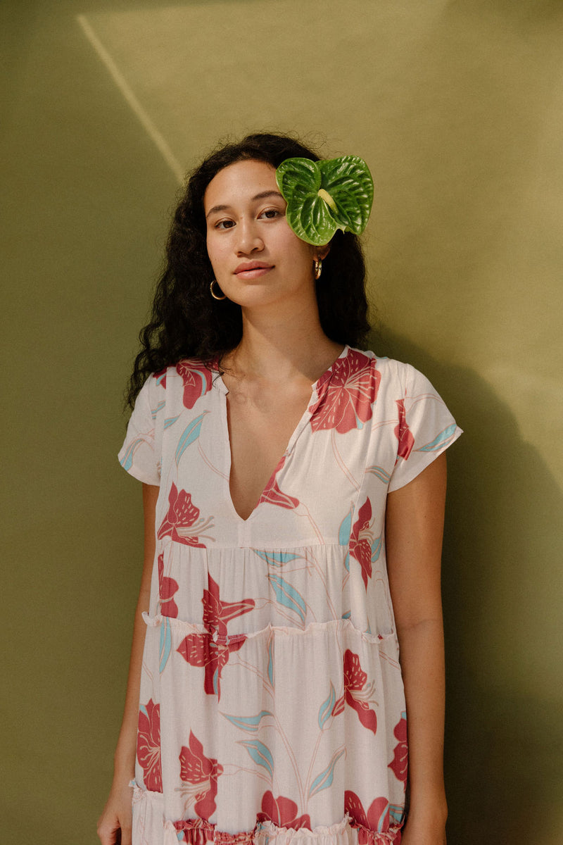 Woman wearing long flowy tiered short sleeve dress with red and light blue floral on beige ground.