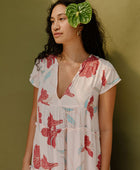 Woman wearing long flowy tiered short sleeve dress with red and light blue floral on beige ground.