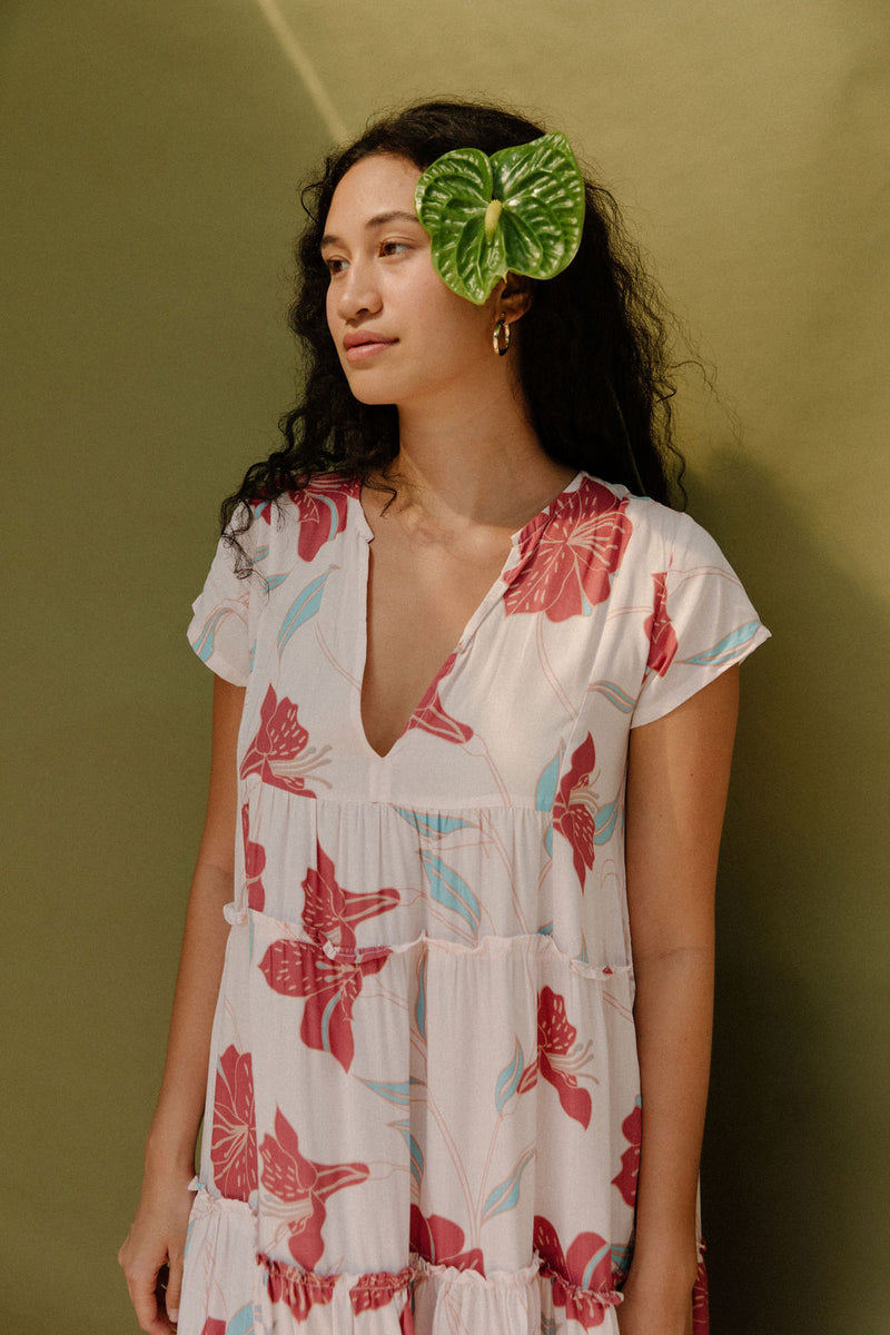 Woman wearing long flowy tiered short sleeve dress with red and light blue floral on beige ground.