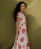 Woman wearing long flowy tiered short sleeve dress with red and light blue floral on beige ground.