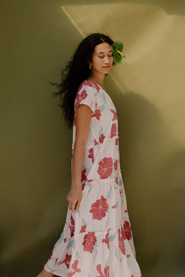 Woman wearing long flowy tiered short sleeve dress with red and light blue floral on beige ground.