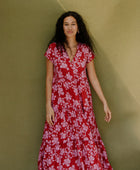 Woman wearing long flowy tiered short sleeve dress with pink floral on red ground.