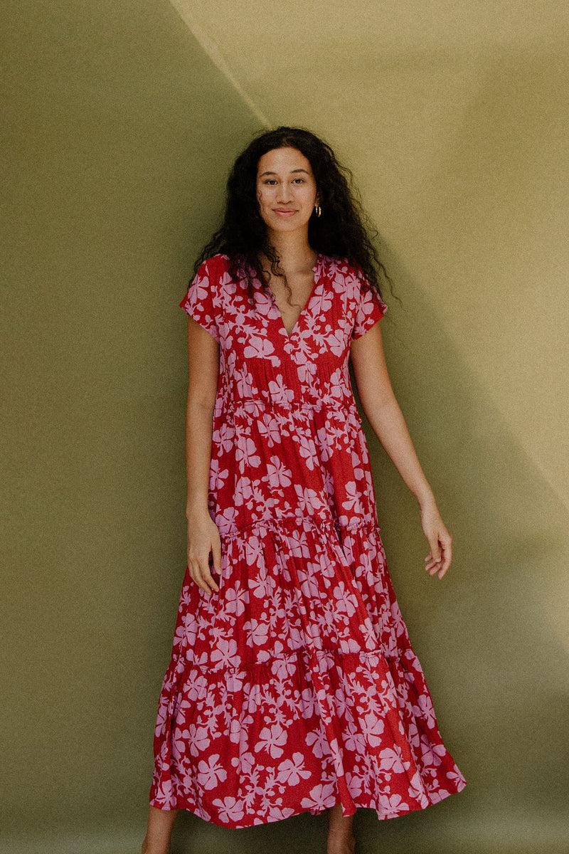 Woman wearing long flowy tiered short sleeve dress with pink floral on red ground.