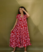 Woman wearing long flowy tiered short sleeve dress with pink floral on red ground.