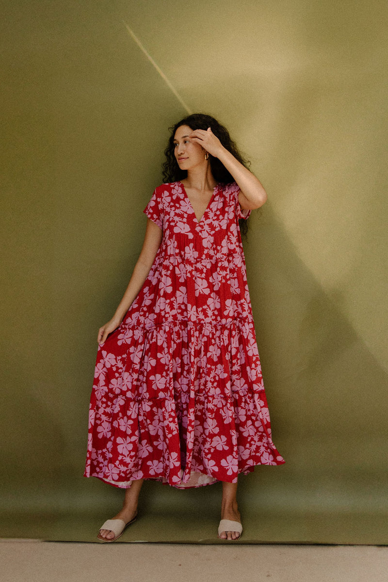 Woman wearing long flowy tiered short sleeve dress with pink floral on red ground.