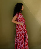 Woman wearing long flowy tiered short sleeve dress with pink floral on red ground.