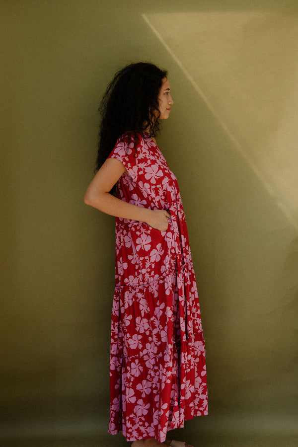 Woman wearing long flowy tiered short sleeve dress with pink floral on red ground.