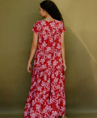 Woman wearing long flowy tiered short sleeve dress with pink floral on red ground.