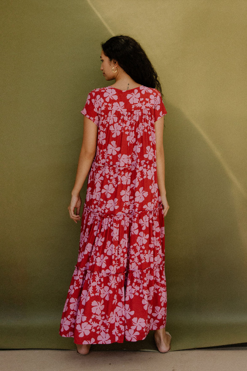 Woman wearing long flowy tiered short sleeve dress with pink floral on red ground.